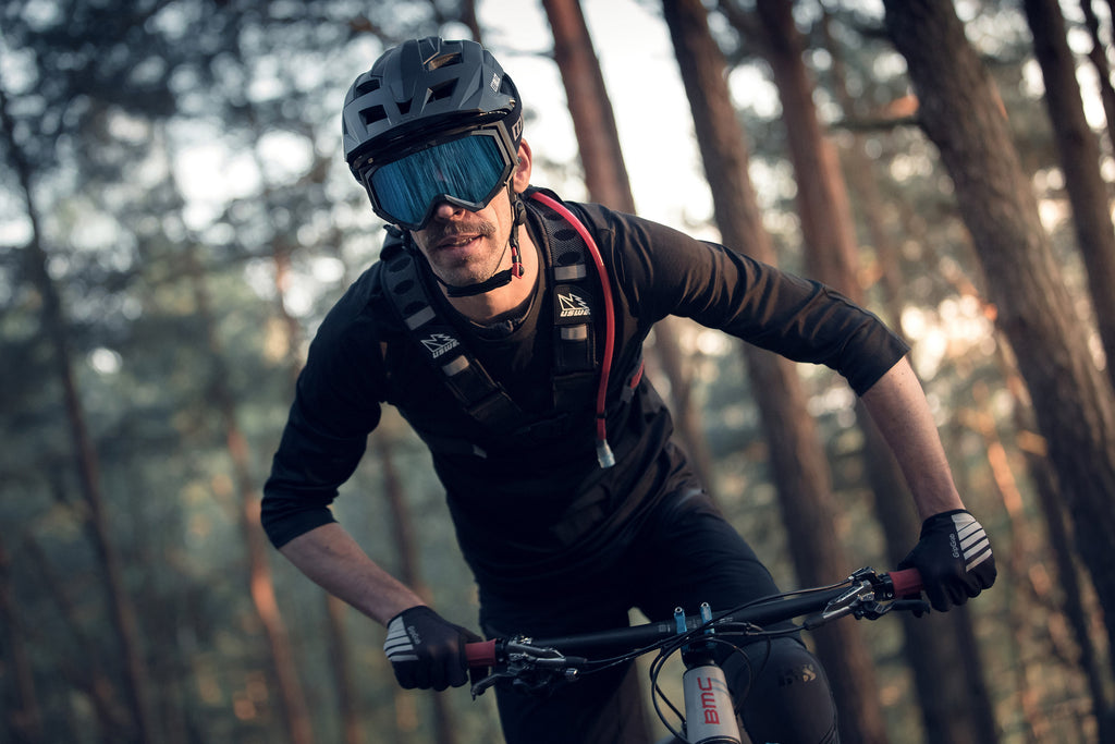 Man wearing black downhill mountain bike protective glasses with blue lens whilst mountain biking in forest