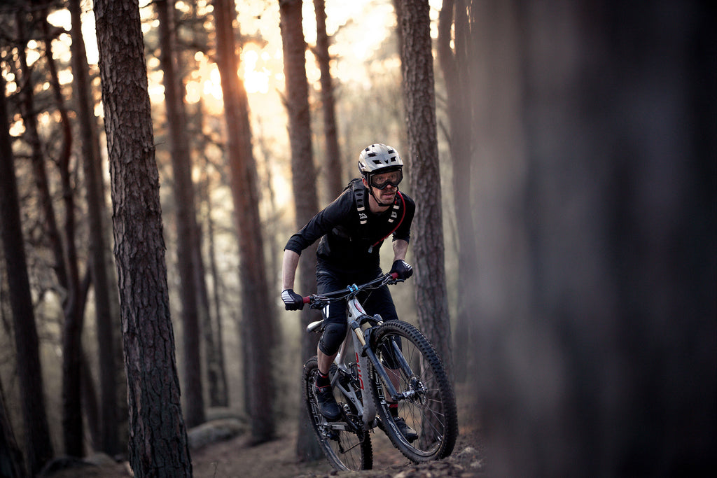 Man wearing black downhill mountain bike protective glasses whils mountain biking through forest