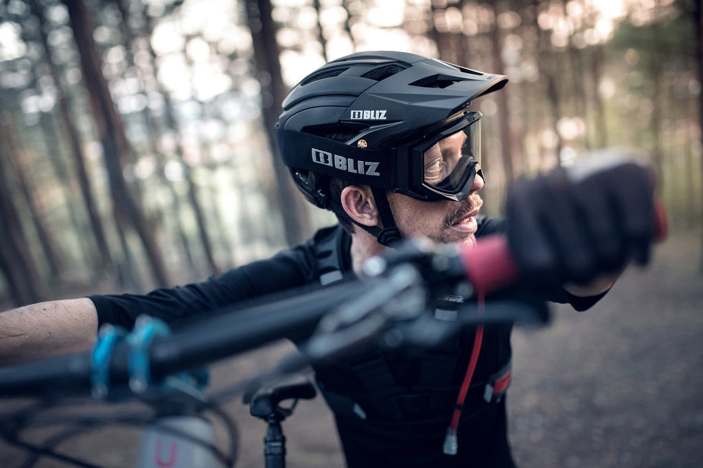 Man wearing black downhill mountain bike protective glasses whilst mountain biking in forest